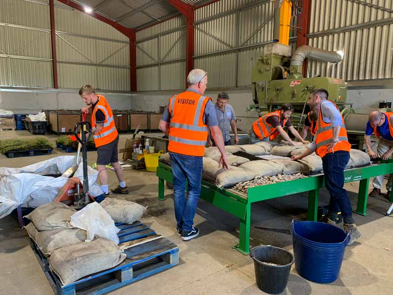 A group of delegates in high vis waistcoats building a demonstration green roof inside an agricultual building